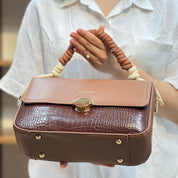 Sac à main avec anse en corde nouée et fermeture métallique.