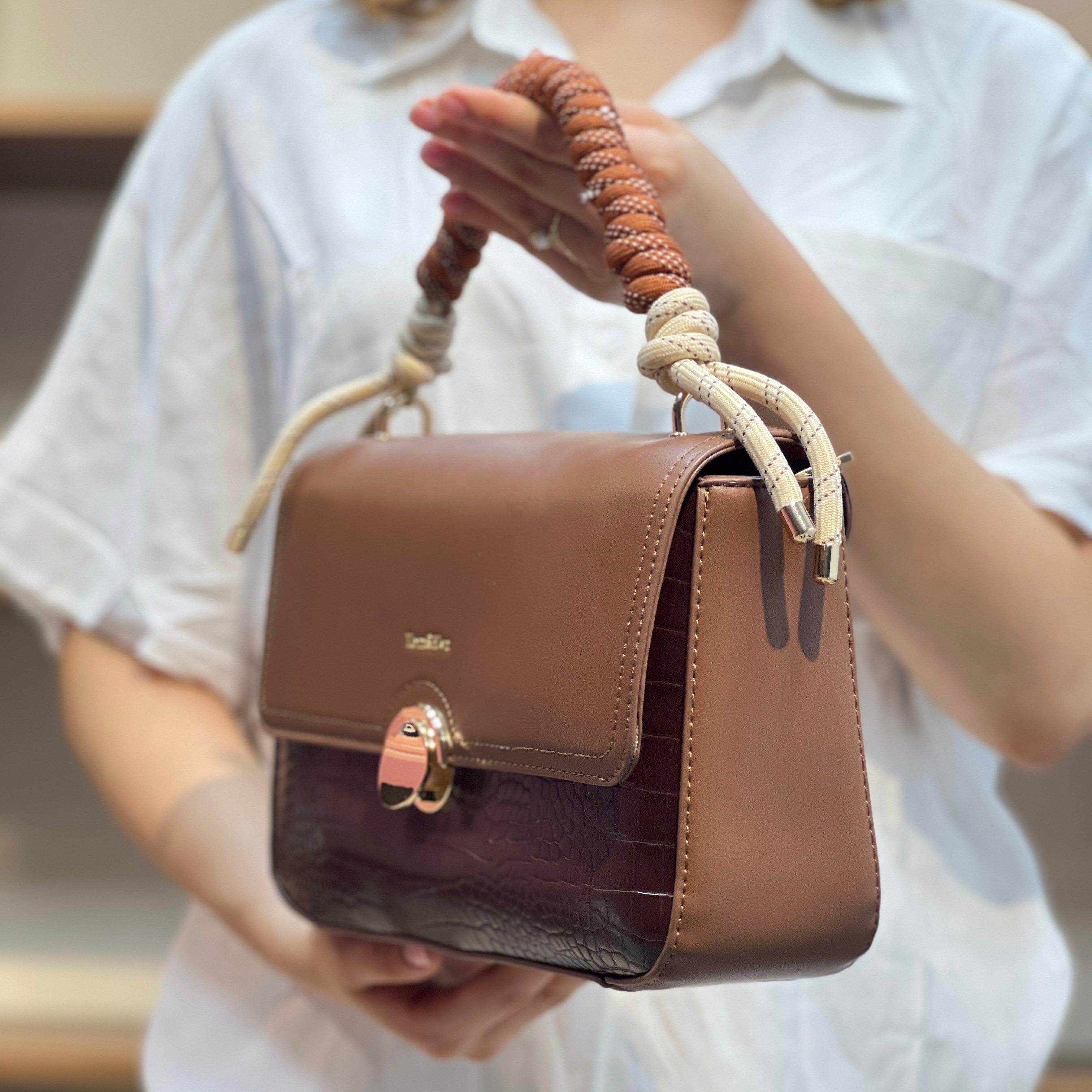 Sac à main avec anse en corde nouée et fermeture métallique.